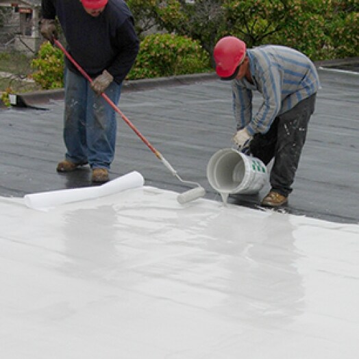 Two Siplast workers pouring and rolling parapro flashing resin