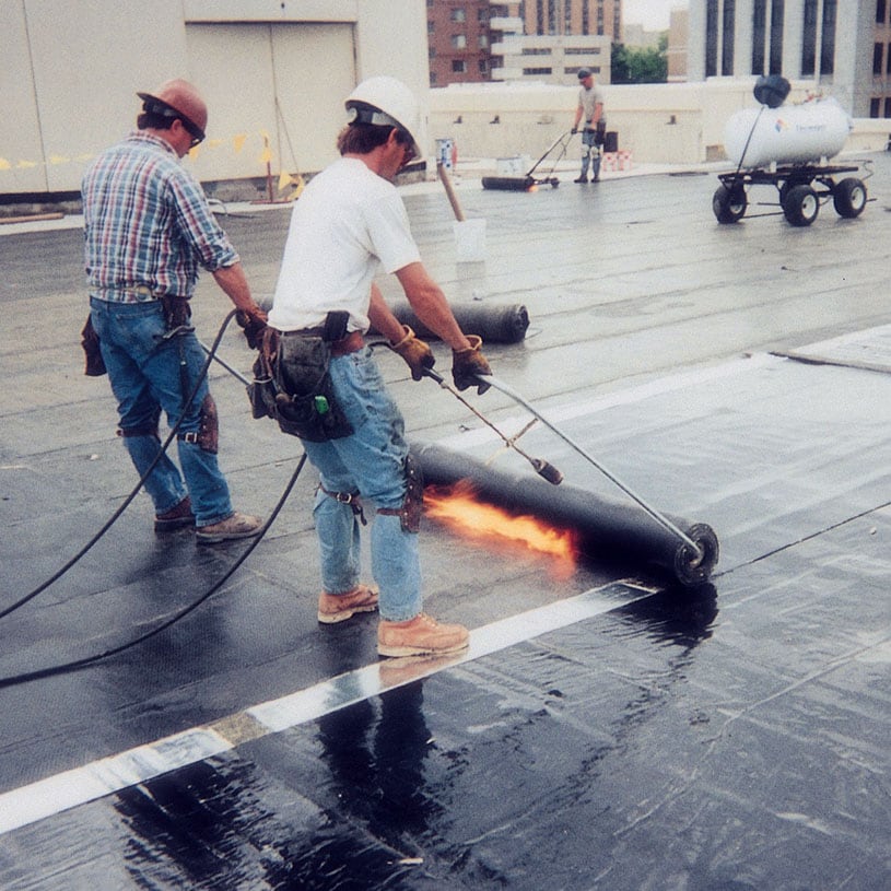 Contractors using torch to apply commercial roofing materials