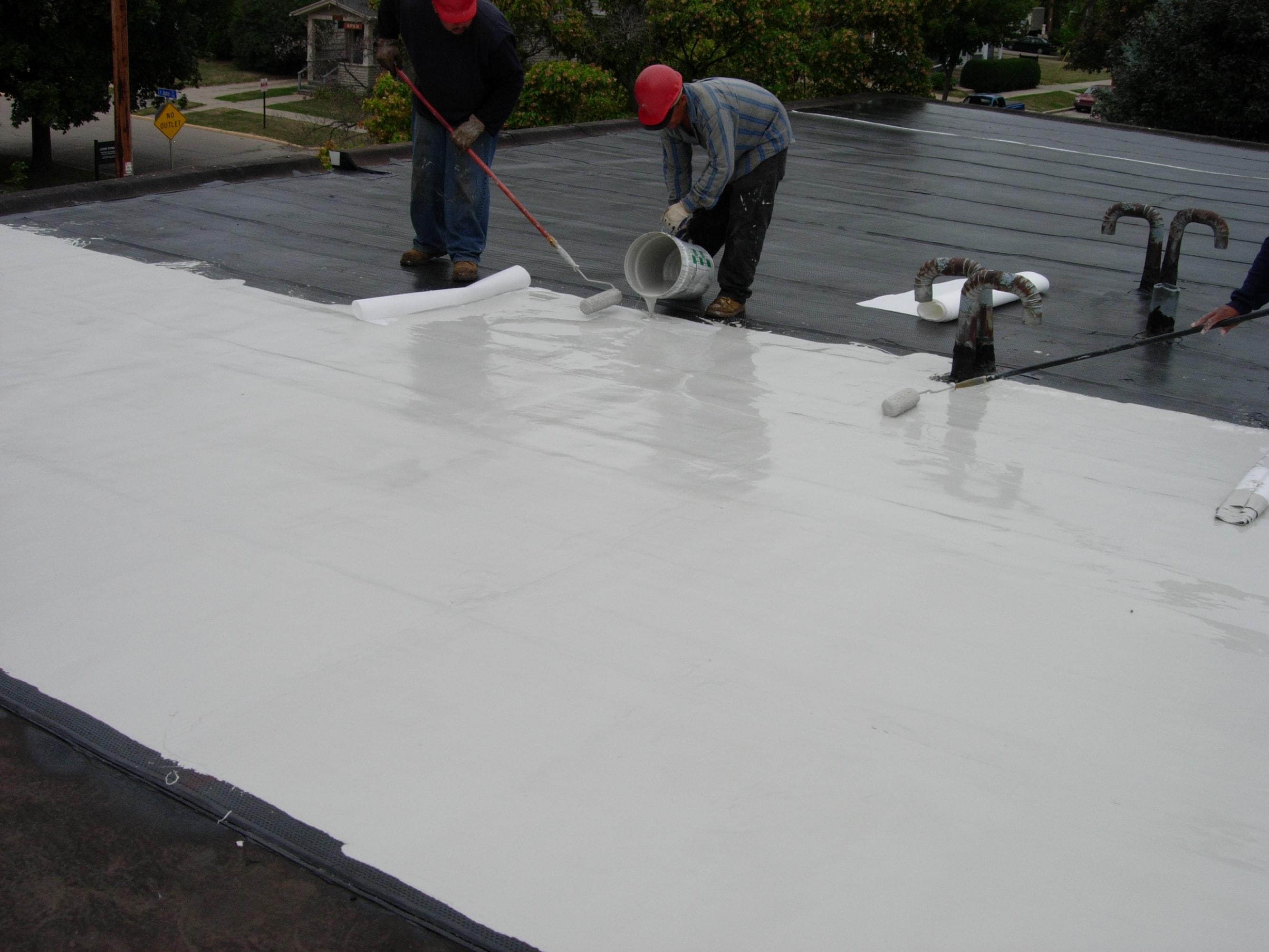 Two Siplast PMMA  seasoned contractors pouring and rolling pmma roof membrane on a roof