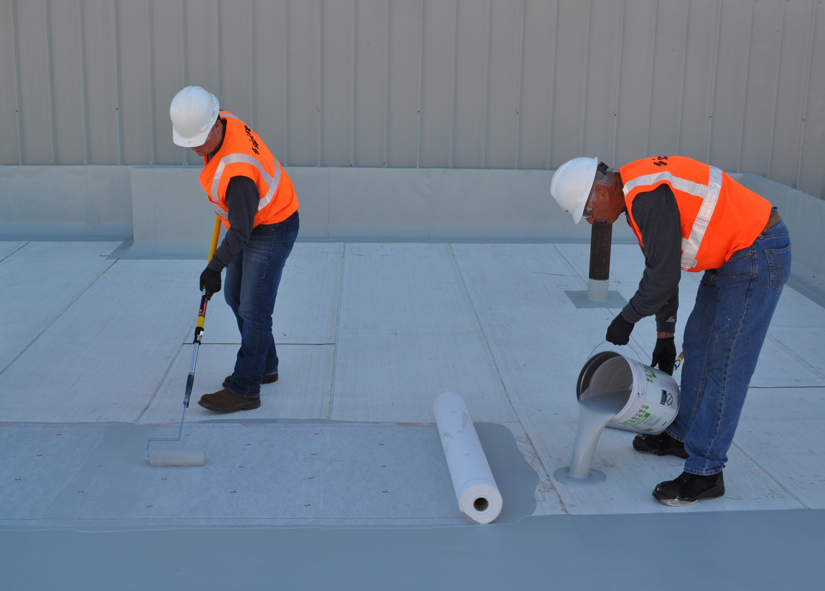 Two Siplast workers pouring and rolling pmma roof membrane